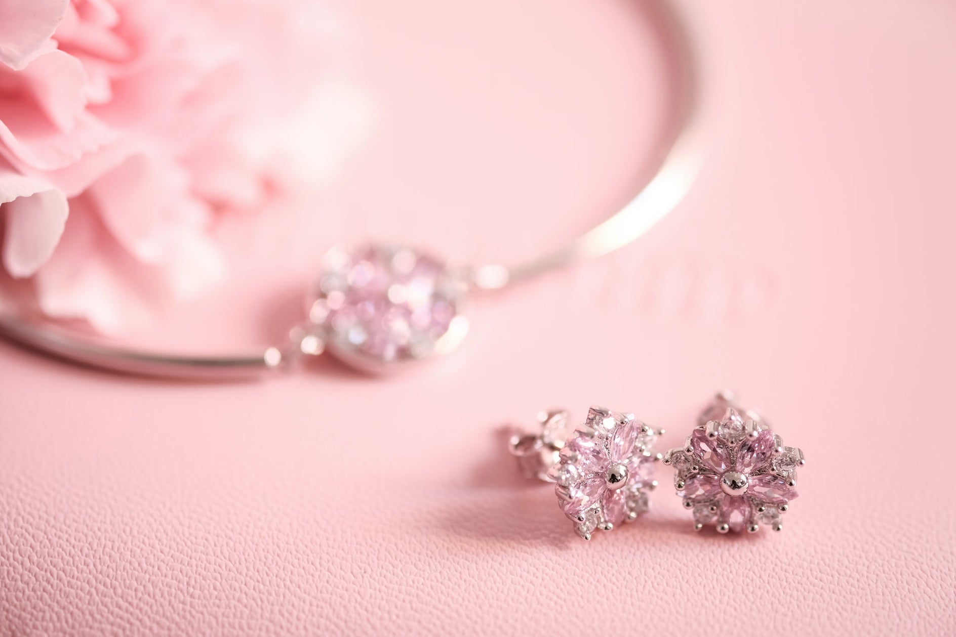 Pair of silver earrings with pink gemstones on a pink background