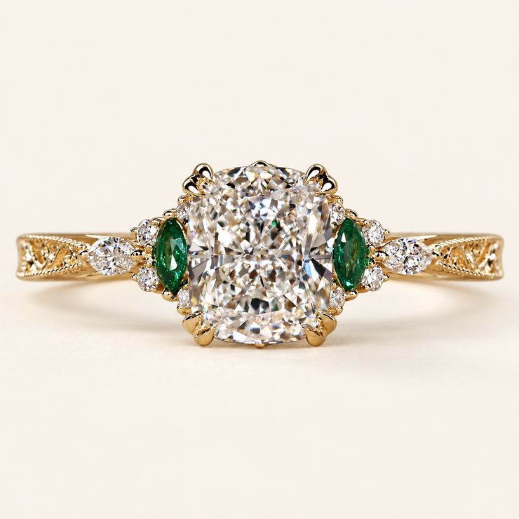 Cushion cut lab grown diamond engagement ring with green marquise emerald gemstones, round diamond accents, decorative filigree and milgrain yellow gold shoulders.