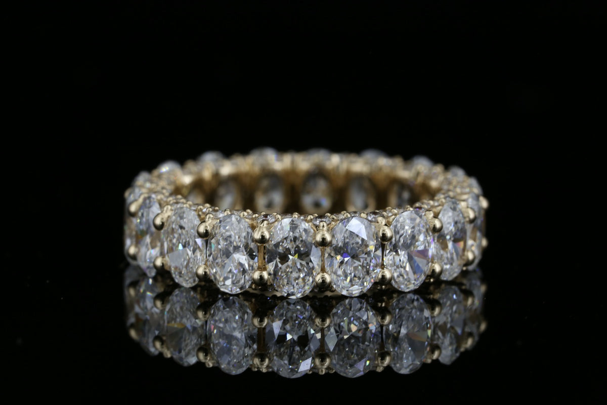 Yellow gold eternity ring with 5.280ct oval lab grown diamonds photographed on black