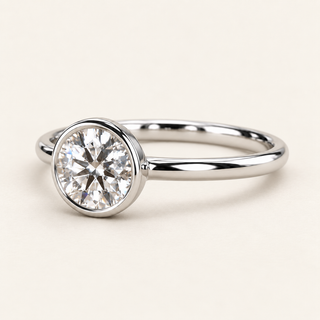 Round lab grown diamond bezel engagement ring in white gold with a continuous polished rim and plain band