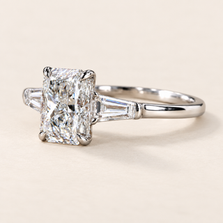 Radiant cut lab grown diamond three-stone engagement ring in white gold with four center prongs, tapered baguette side diamonds and polished shank.