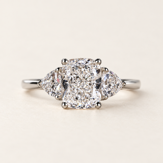 Cushion cut lab grown diamond three-stone engagement ring with 1.50 ct center diamond, two trillion cut side diamonds and polished yellow gold band.