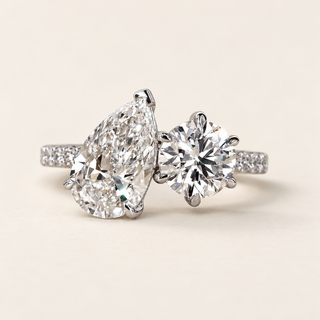 Pear cut lab grown diamond two-stone engagement ring with 2.00 ct pear, 1.25 ct round diamond, raised open baskets and pavé shoulders in white gold.
