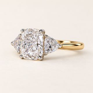 Cushion cut lab grown diamond three-stone engagement ring with 1.50 ct center diamond, two trillion cut side diamonds and polished yellow gold band.