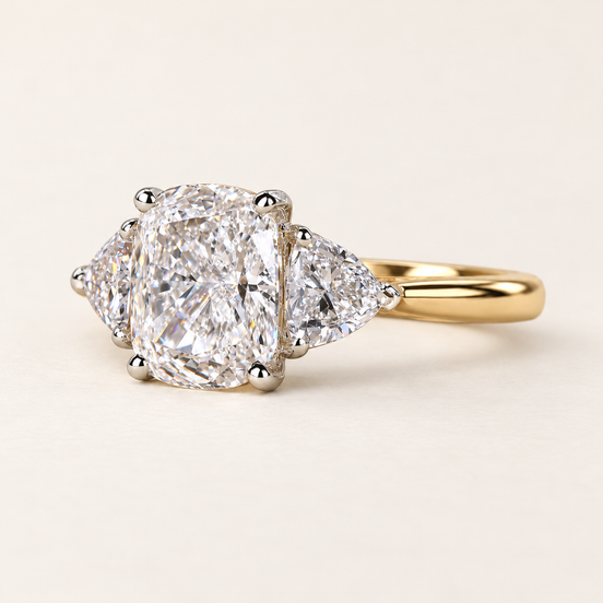 Cushion cut lab grown diamond three-stone engagement ring with 1.50 ct center diamond, two trillion cut side diamonds and polished yellow gold band.