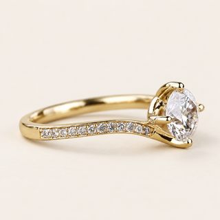 Round cut lab grown diamond bypass engagement ring in yellow gold with four-prong center, asymmetrical pavé shoulders and sweeping twist band.